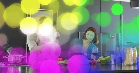 Couple cooking and laughing at modern kitchen island with wine, salad and colorful bokeh