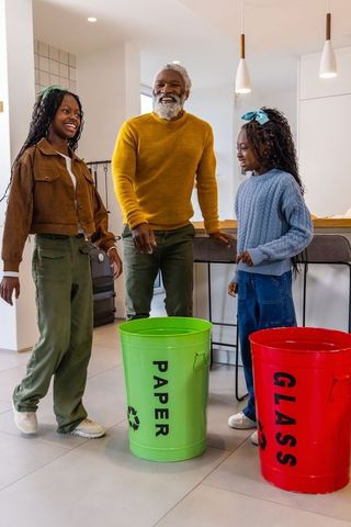 African american grandfather teaching granddaughters recycling, sorting paper and glass