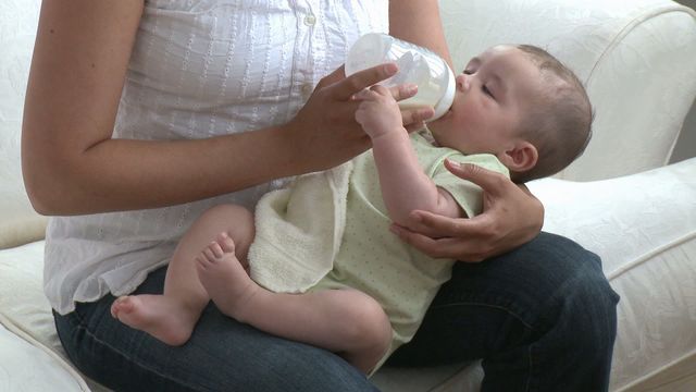 Shows a mother feeding her baby with a bottle while sitting on a comfortable sofa. Ideal for use in parenting articles, childcare blogs, or infant nutrition guides to depict nurturing and bonding between parent and child. Could also be used in promotional materials for baby products or family magazines.