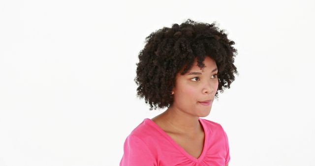 A young African American girl looks to the side with a thoughtful expression, with copy space. Her casual pink top adds a bright touch to the simple background, suggesting a relaxed atmosphere.