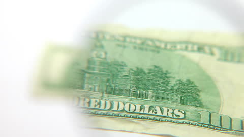 Magnifying Glass Hovering Over US Dollar Note for Detailed Examination