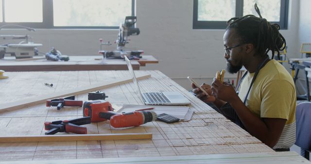 African American man reviews plans at a workshop. His focus on the laptop and project suggests careful planning in a creative space.