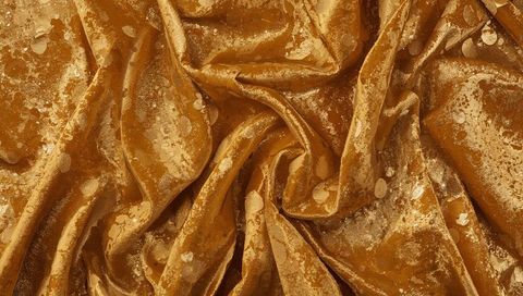 Luxurious golden crushed velvet with metallic splatter and glossy sheen, dramatic swirled folds