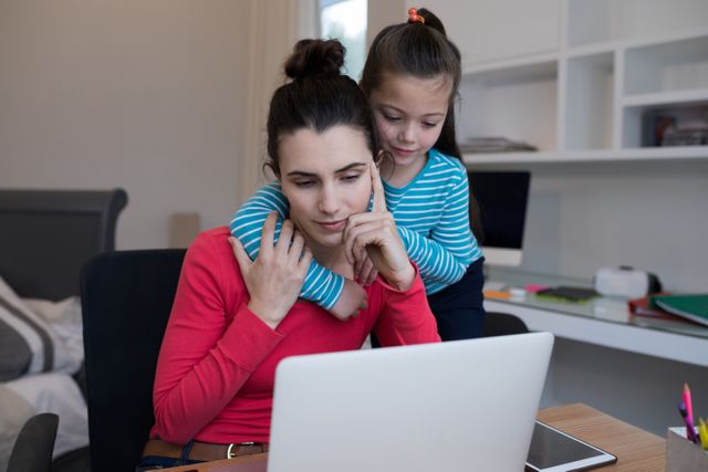 Mother and daughter using laptop at desk in home