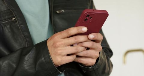 Mid adult man typing on red smartphone wearing black leather jacket closeup