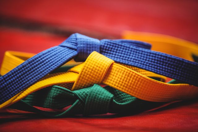 This image shows a close-up of blue, yellow, and green karate belts placed on a red surface. The belts are neatly tied, representing different levels of achievement in martial arts. This image can be used for promoting martial arts classes, illustrating articles about karate, or as a visual aid in sports and fitness-related content.