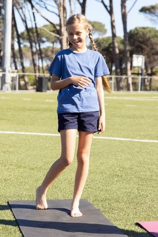 Young girl practicing barefoot balance on turf, smiling during outdoor kids fitness session