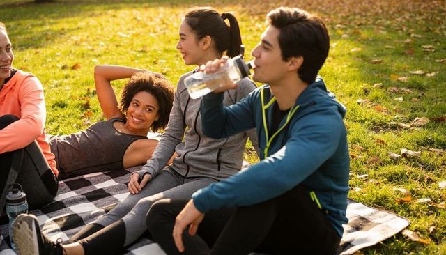 Friends relaxing on checkered blanket after outdoor workout in sunlit autumn park