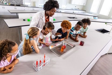 African american female teacher leading hands-on chemistry demo with young students in school lab
