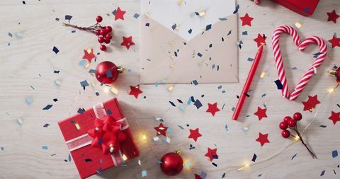 Festive flatlay featuring red gift box, candy cane heart and envelope on light wood with confetti