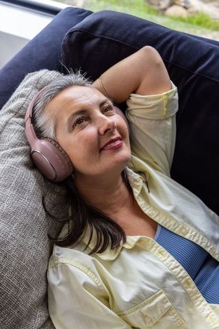Middle-aged woman reclining and listening to music on pink wireless headphones