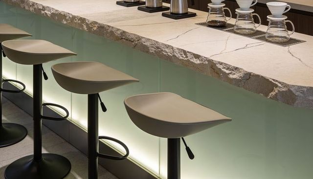 Modern backlit bar counter featuring rough-cut stone edge and three minimalist swivel stools