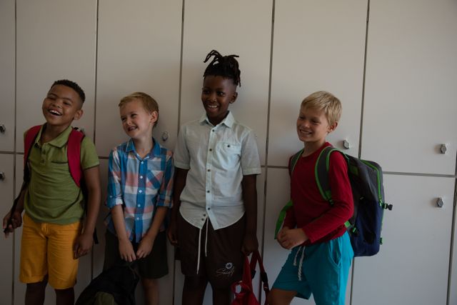 Group of multiracial elementary schoolboys standing by lockers, smiling and holding backpacks. Ideal for educational materials, diversity and inclusion campaigns, back-to-school promotions, and childhood friendship themes.