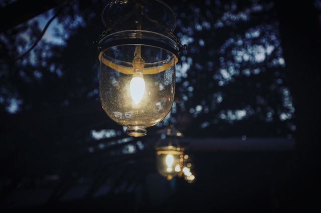 Outdoor scene of vintage glass lanterns hanging and lit while setting a comforting and cozy evening ambiance. Suitable for use in content related to outdoor decor, evening events, cozy settings, rustic ambiance, and vintage lighting options.