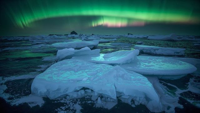 Aurora reflecting on fractured ice floes over polar ocean, glowing turquoise night sky
