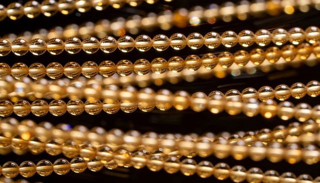 Shimmering golden bead strands in parallel rows macro amber glossy reflective bokeh jewelry