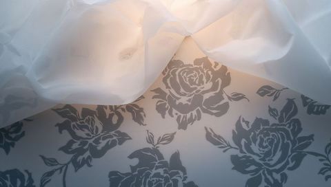 Sheer curtain filtering light over gray rose wallpaper creating soft floral ambience