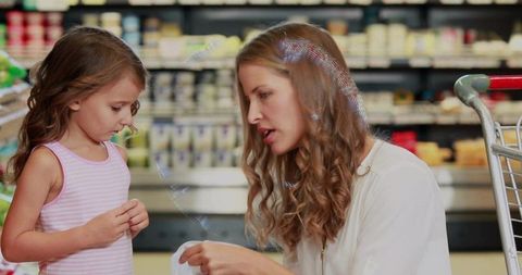 Mother explaining receipt to daughter while grocery shopping in supermarket dairy aisle