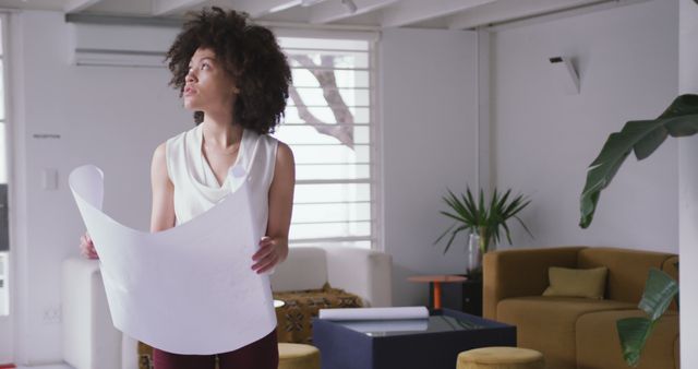 Young female architect studying blueprints in bright and modern office. Perfect for ads, articles, website headers, or stories related to architecture, design, professional work environments, and creative planning. Highlights a blend of modern work culture and innovative thinking.