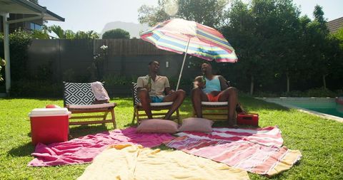 Friends Relaxing in Backyard under Colorful Umbrella during Sunny Day