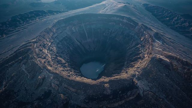 Aerial revealing vast circular caldera with layered strata and turquoise crater lake