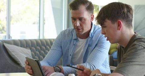 Parent teaching teen using tablet in modern living room with natural light