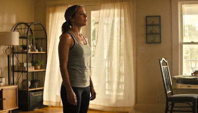 Woman in activewear standing by sunlit sheer curtains, home wellness lifestyle portrait