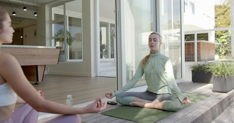 Women meditating on modern home deck practicing outdoor yoga, mindfulness and relaxation