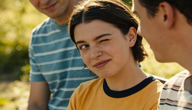 Winking young woman sharing laugh with friends while chatting in sunny park