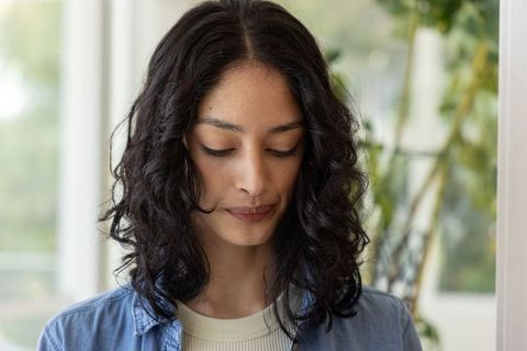 Asian woman gazing downward in sunlit interior, contemplative closeup portrait headshot