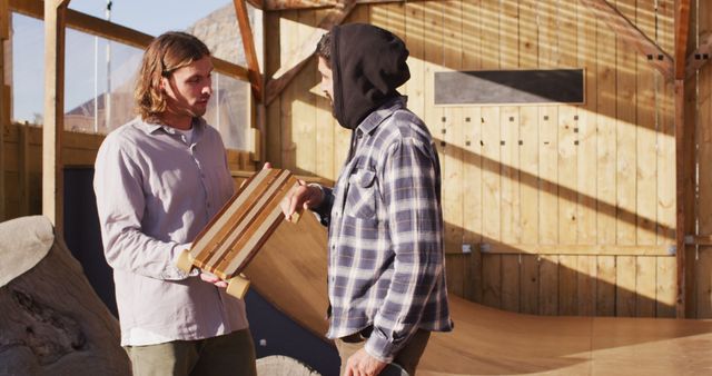 Two men are seen in a skatepark workshop. One is holding a wooden skateboard while they have a focused discussion. This scene is ideal for illustrating themes of craftsmanship, sports, and teamwork. It can be used in advertisements for skateboarding brands, DIY and hobbyist communities, or articles about custom skateboard making.