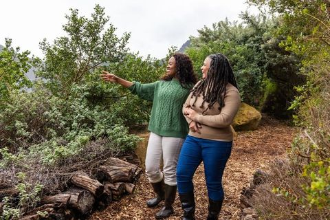 Two african american women walking forest trail pointing and laughing in casual boots