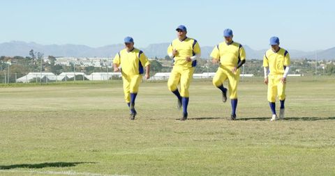 Male baseball teammates running warm-up drill in yellow uniforms on grassy field