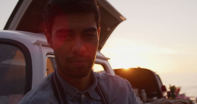 Young man standing next to a car while watching the sunset, suggesting a moment of relaxation and leisure. Ideal for travel, adventure, or lifestyle projects showcasing enjoying nature and outdoor activities.