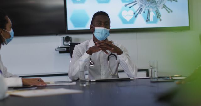 African american male doctor wearing mask giving presentation in meeting room. medical professionals at work during covid 19 coronavirus pandemic.