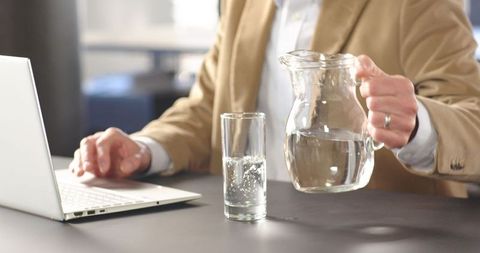 Businessman pouring water while working on laptop