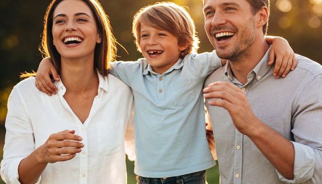 Laughing family embracing son during golden-hour outdoor portrait, parents enjoying moment