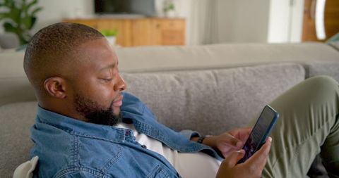 Adult man reclining on sofa using smartphone for messaging and relaxation at home