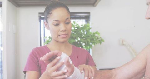 Caregiver wrapping wrist bandage on senior patient in clinic, nurse providing first aid care