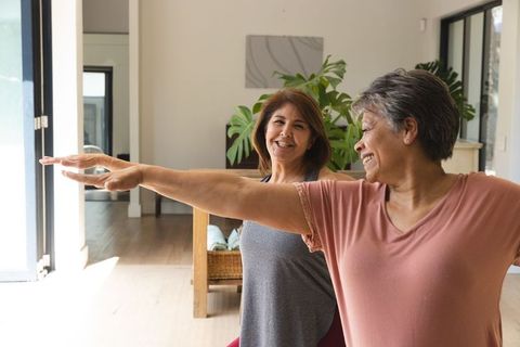 Senior women practicing yoga warrior ii pose in bright living room