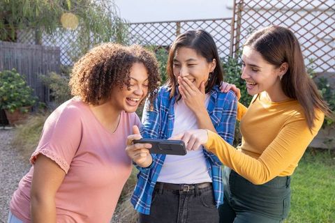 Diverse Friends Laughing Together over Smartphone Outdoors