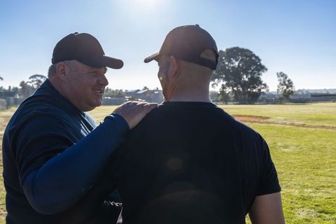 Coach guiding teammate on sunny baseball field, mentoring strategy during early practice