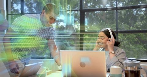 Man assisting woman adjusting headset while collaborating at laptop in coworking space