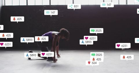 Crouching female athlete preparing sprint amid floating social notifications in industrial studio
