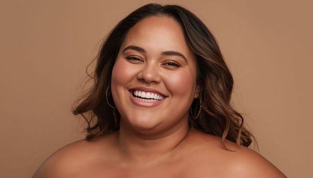Smiling hispanic woman wearing gold hoop earrings and warm makeup, bare-shouldered portrait