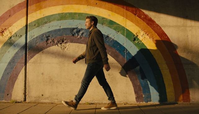 Man walking past rainbow mural at golden hour urban street style shadow silhouette