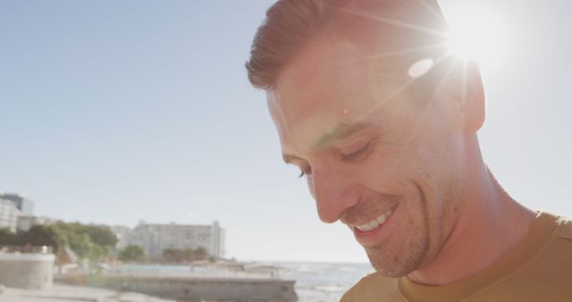 Man smiling while enjoying a sunny day at the beach, ideal for vacation or leisure concepts. Perfect for promoting outdoor activities, nature exploration, relaxation, travel, and summer fun. Use in travel brochures, websites, advertisements, or social media posts to highlight happiness and cheerful moments.