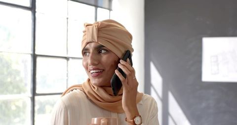 Indian woman using smartphone in modern office with coffee