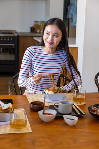 Young Asian Woman Enjoying Noodles at Home in Cozy Kitchen
