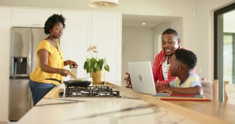 African American family cooking while dad and son working on laptop at kitchen island